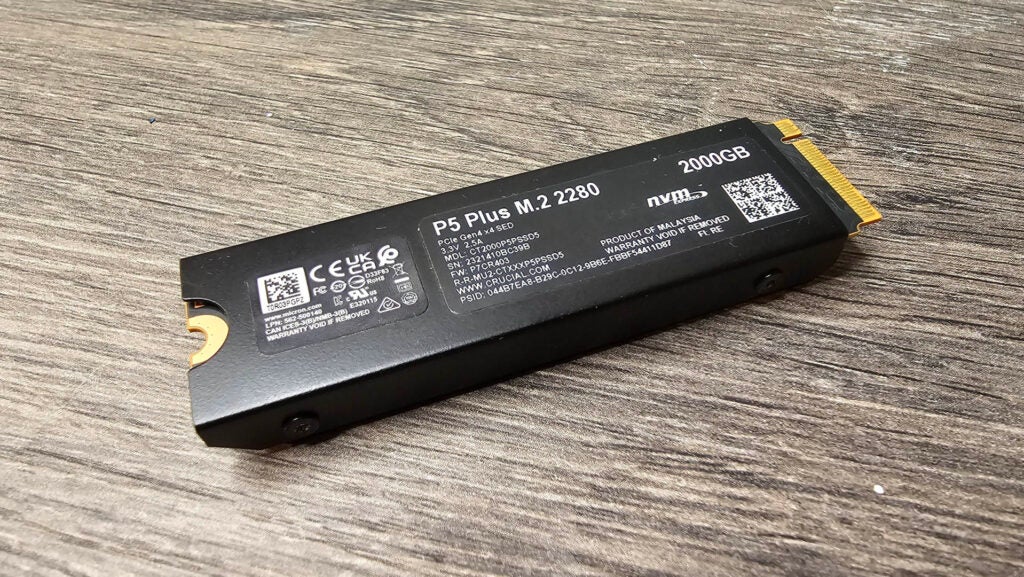 Die Rückseite des Kühlkörpers der P5 Plus M.2 PCIe 4.0 SSD von Crucial. Crucial P5 Plus M.2 PCIe 4.0 SSD 2 TB auf einer Holzoberfläche.