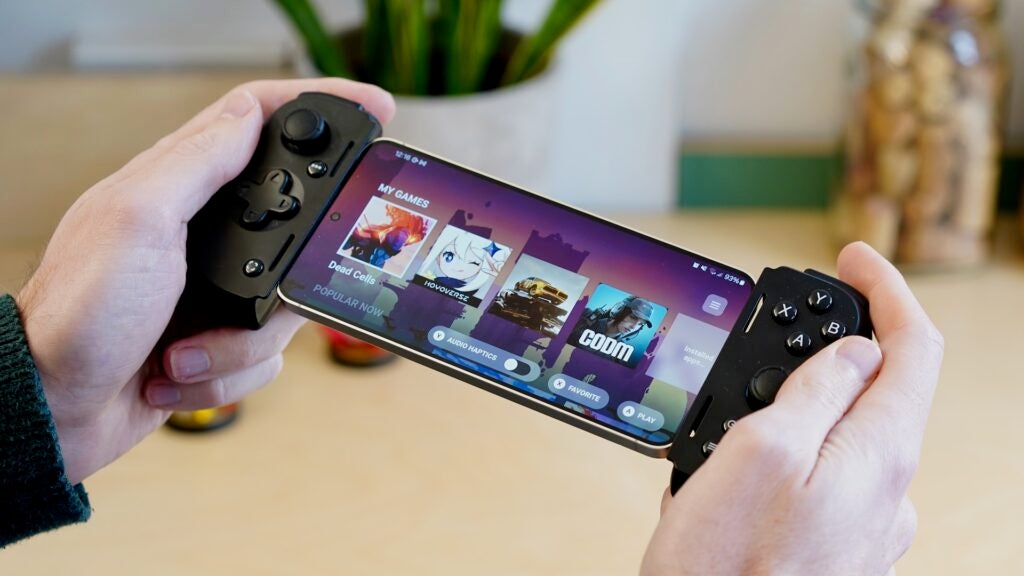 Hände halten das Razer Kishi V2 Pro, das an ein Smartphone angeschlossen ist, auf dem Spiele angezeigt werden.