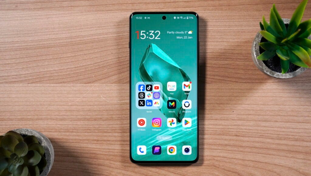 Smartphone OnePlus 12 sobre superficie de madera con pantalla encendida.