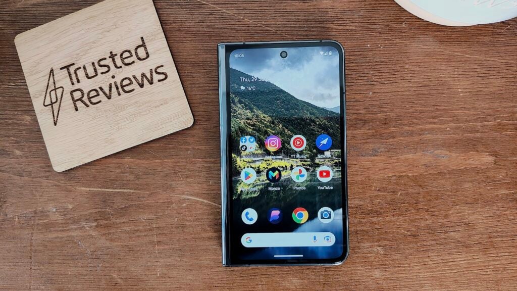 Google Pixel Fold junto a un posavasos de Themelocal sobre una mesa de madera.