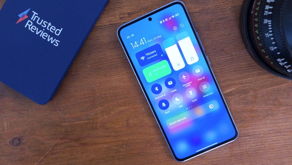 Smartphone Xiaomi 13T Pro sobre una superficie de madera junto a la lente de la cámara.