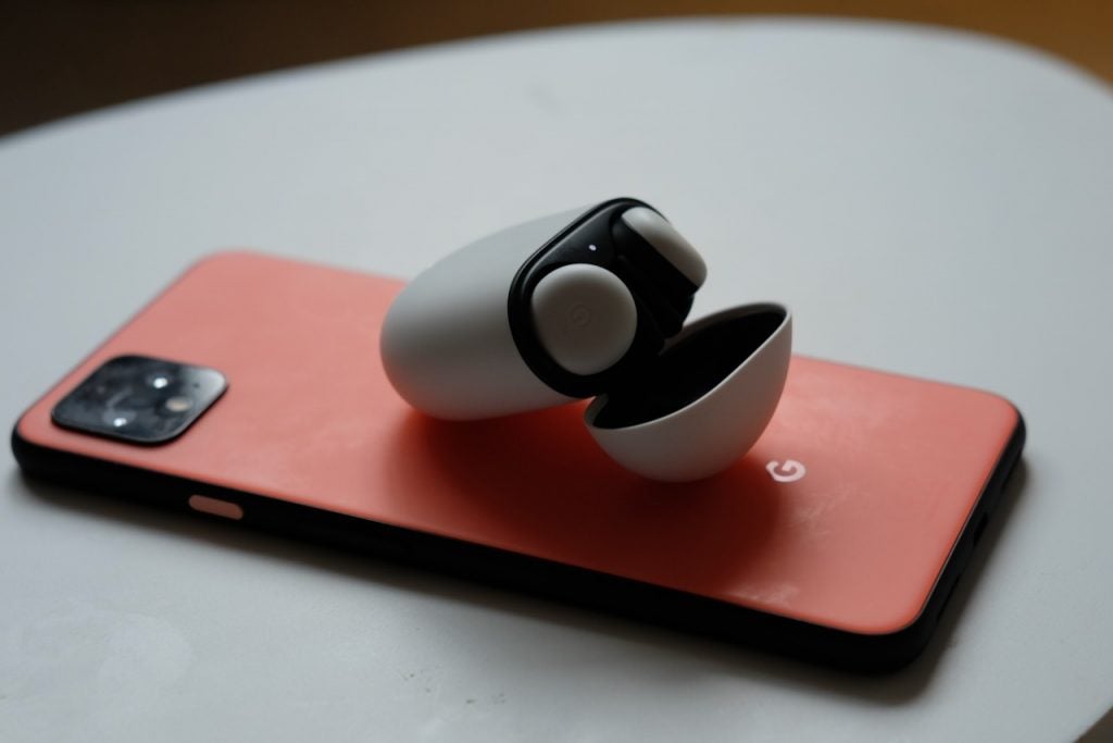 Auriculares Pixel blancos y negros colocados en su estuche sobre un teléfono inteligente Pixel colocado sobre una mesa