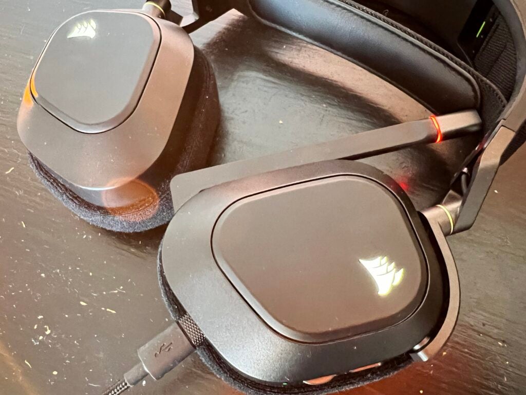 Le logo des oreillettes Corsair allumé sur le casque HS80 RGB posé sur un bureau