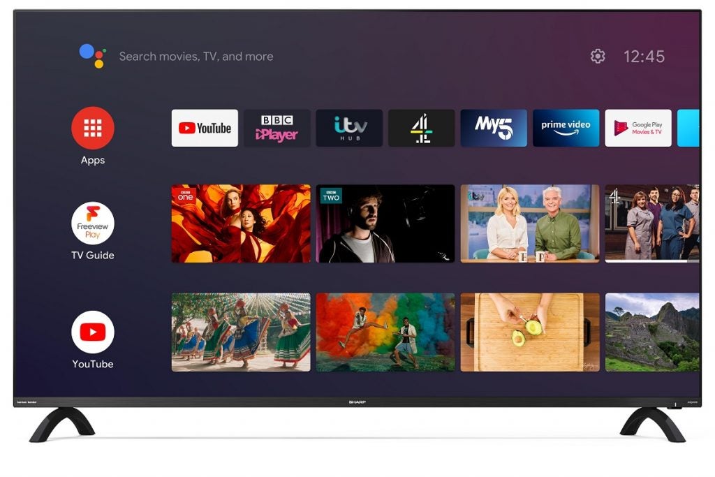 Téléviseur Sharp 65DL2KA avec support affichant les applications, le guide TV et la section youtube avec un bouton de réglage en haut à gauche et la barre de recherche de l'assistant Google en haut à droite